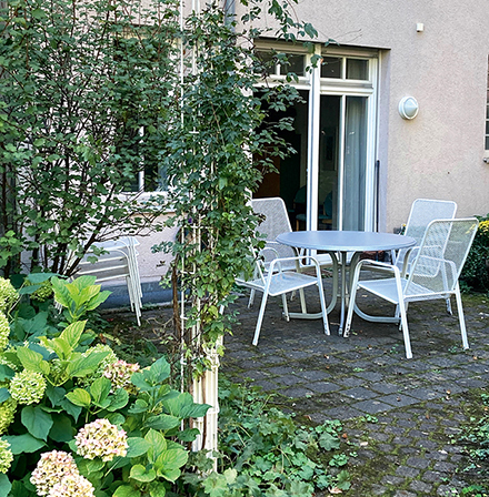 wg1: Blick vom Garten auf die Terrasse mit Gartenstühlen vor dem Eingang zum Gemeinschaftsraum